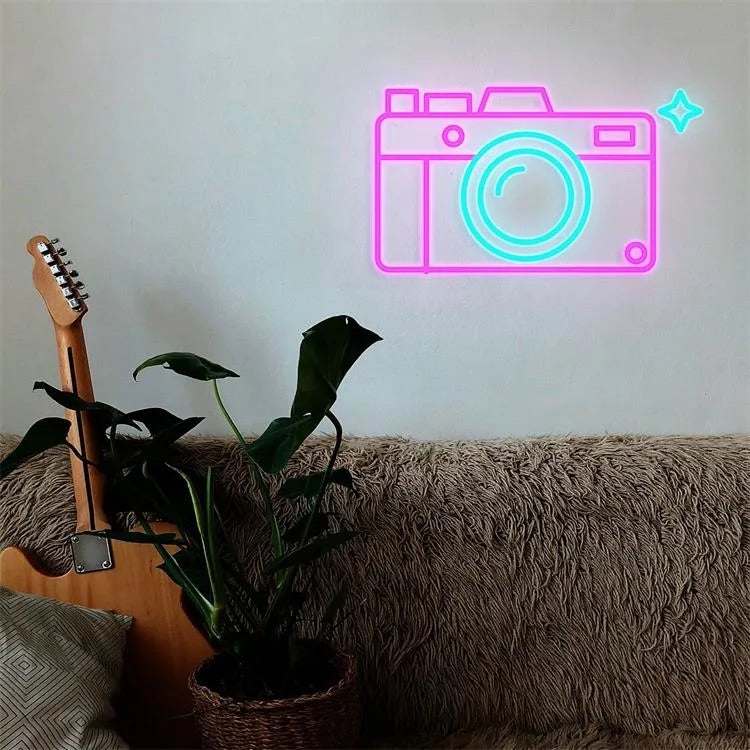 Neon camera sign mounted on wall above couch with guitar and plant nearby