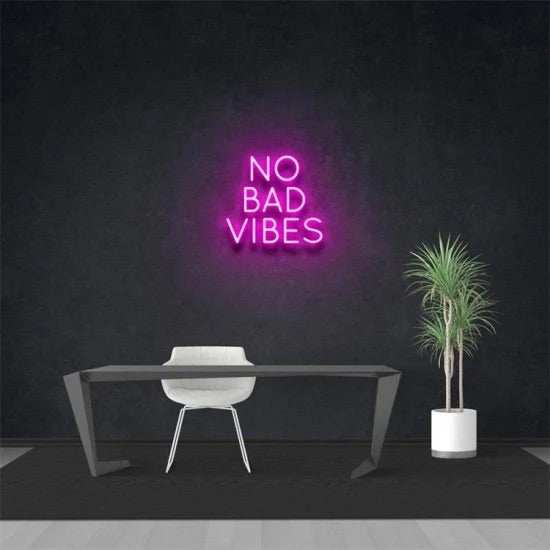 no bad vibes neon sign in pink on black wall above modern desk with chair and potted plant