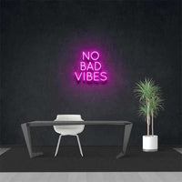 no bad vibes neon sign in pink on black wall above modern desk with chair and potted plant