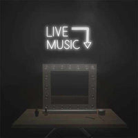 Neon sign reading "LIVE MUSIC" with arrow on dark wall, mounted on plexiglass support above a wooden table.