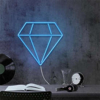 Blue diamante neon light mounted on wall above desk with book, headphones, clock, and vinyl record